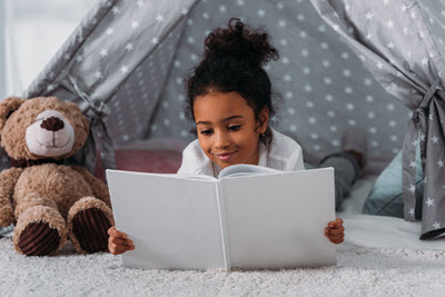 A girl reading a book in her tent with her teddy