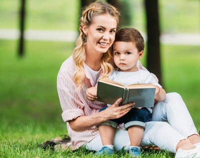 3 year old boy reading outside in the park with his mom