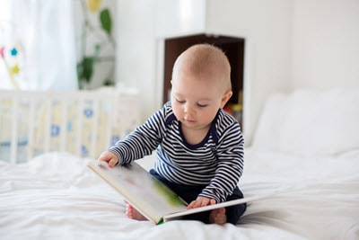 a young baby sitting on the bed and reading a book