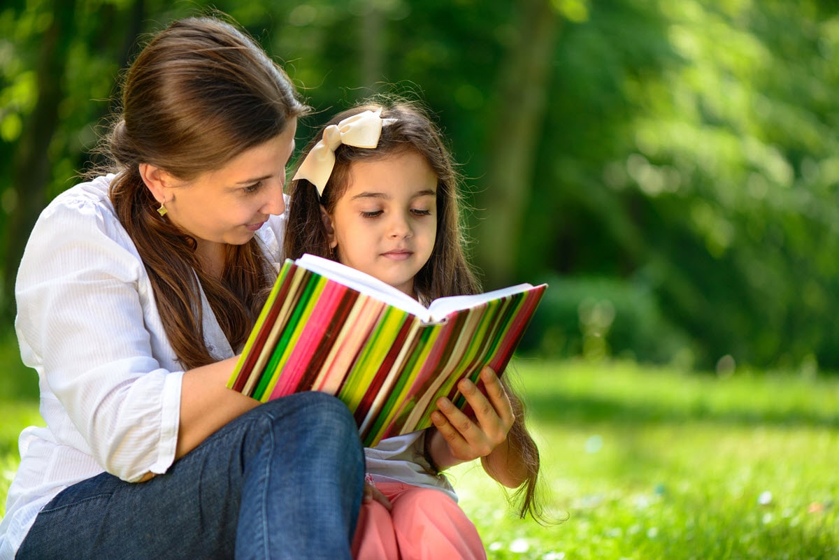 The featured image for the article on how to teach a 6 year old to read showing a mother and daughter reading in a park