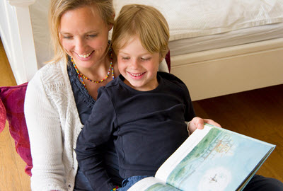 A first-grader sitting on his mother's lap while she reads a storybook to him