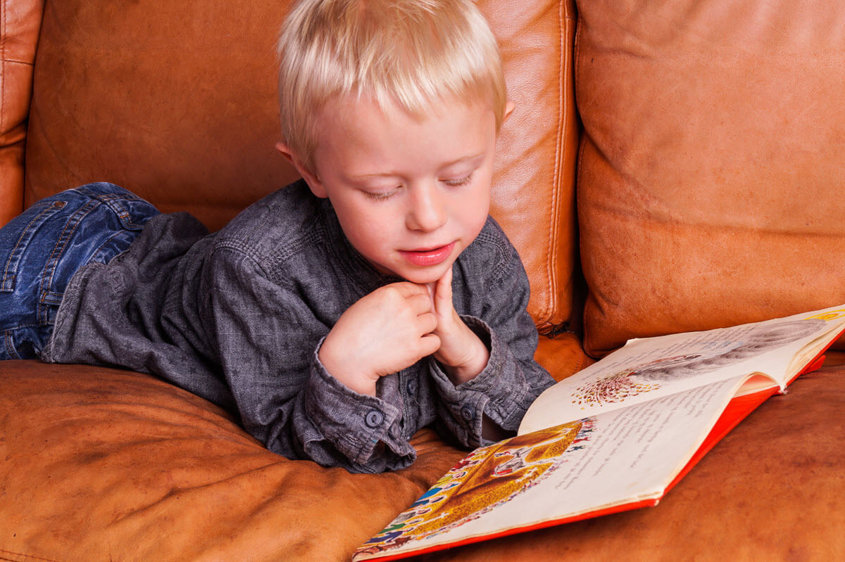 best books for 3-4 year olds featured image showing a boy laying on the sofa and reading a story book