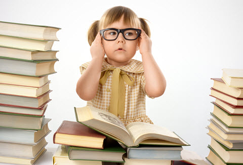 A 6-year old girl with glasses surrounded by stacks of books