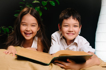 siblings having fun while reading a book aloud to each other
