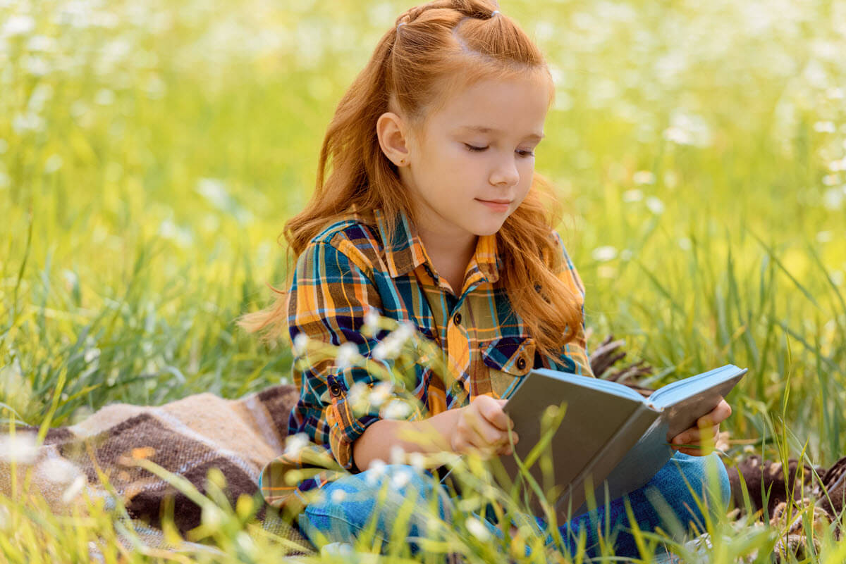 What is fluency in reading featured image of a girl sitting in a field while reading her story book