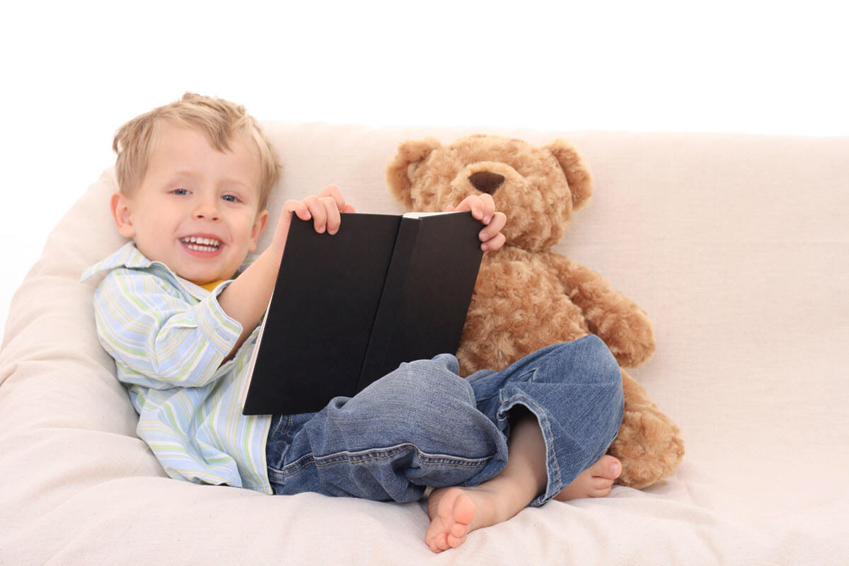 Benefits of reading for young children featured image of a 3 year old boy sitting on the sofa reading a book to his teddy