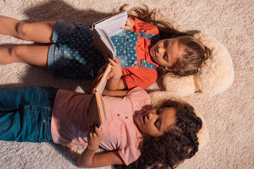two little girls laying on the floor reading books