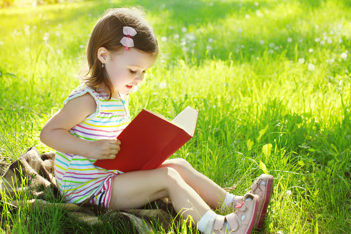 Phonemic awareness vs letter sound correspondence featured image of a young girl sitting outside while reading her book on a summer's day